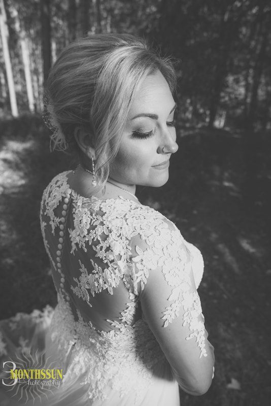 A black and white photo of a woman in a wedding dress standing in the woods.