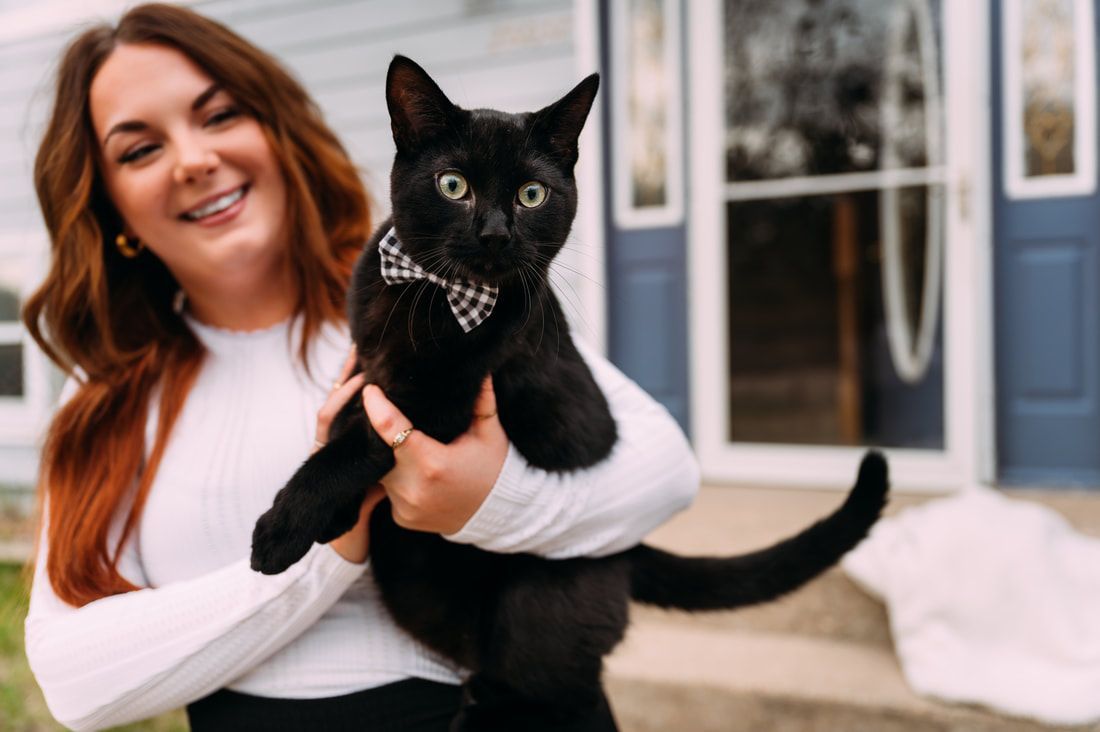 A woman is holding a black cat in front of a house.