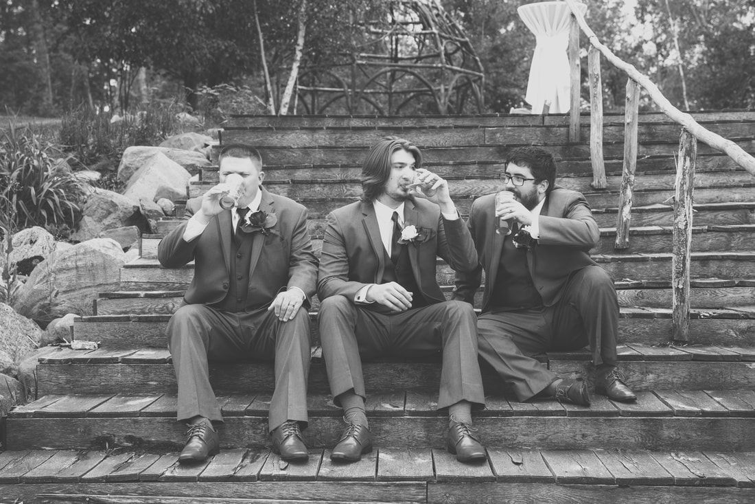 Three men in suits are sitting on wooden steps drinking beer.