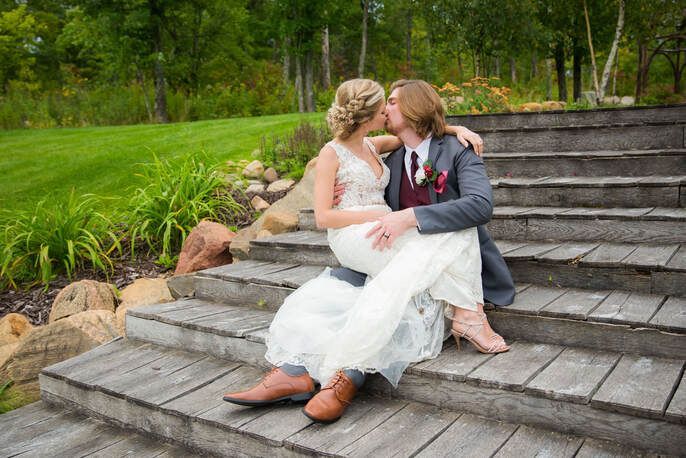 A bride and groom are kissing while sitting on a set of wooden stairs.
