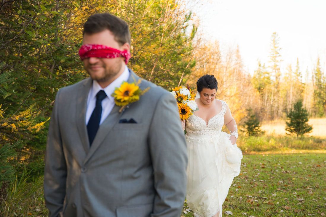 A bride and groom are walking in a field with blindfolds on their eyes.