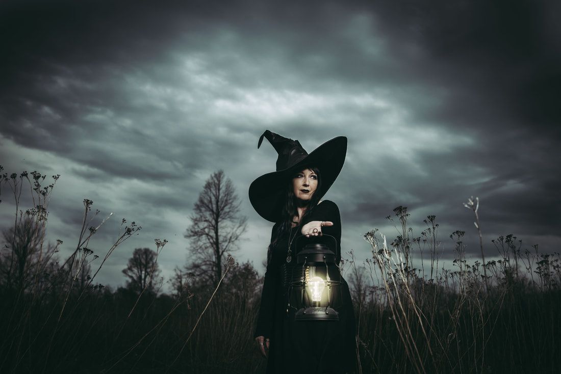 A woman dressed as a witch is holding a lantern in a field.