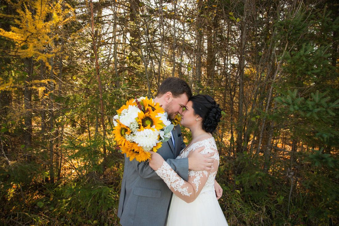 A bride and groom are kissing in the woods while holding a bouquet of sunflowers.