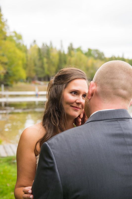 A bride and groom are looking at each other in front of a lake.