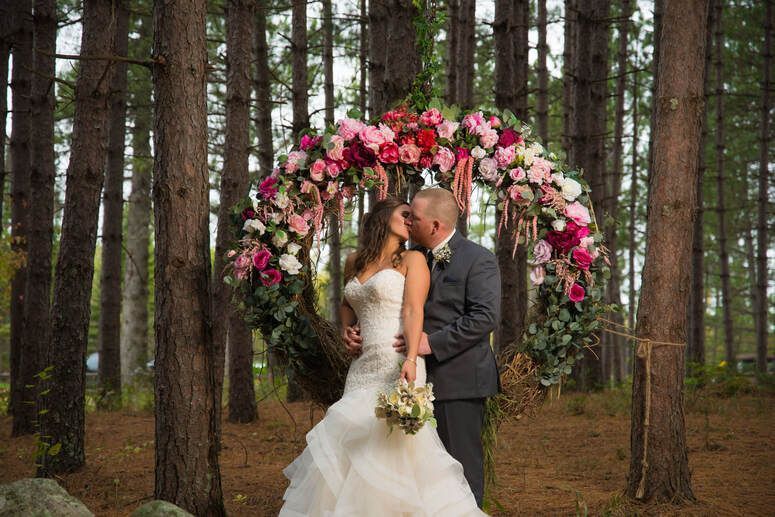 A bride and groom kissing under a floral arch in the woods.