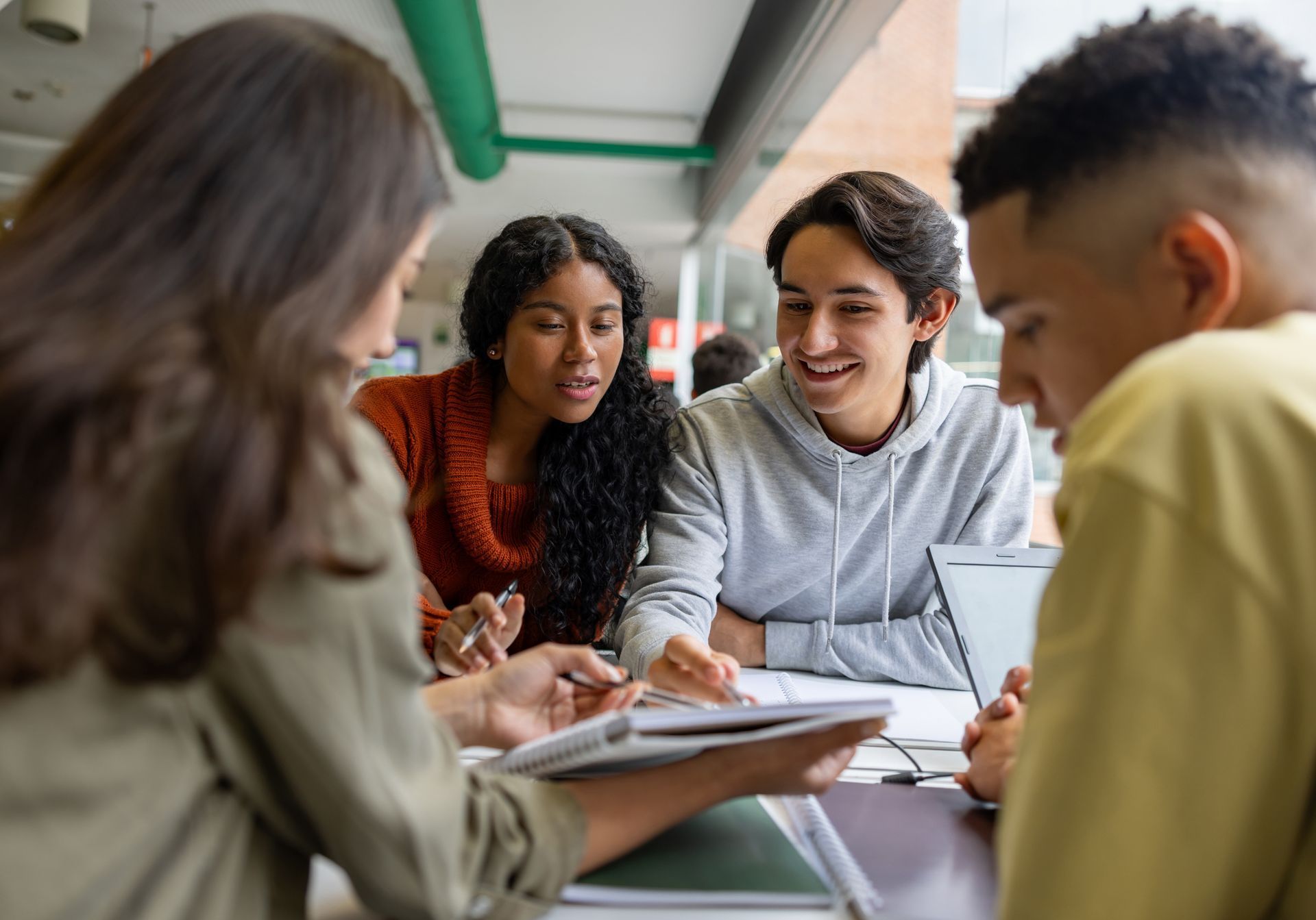 Small group of students gathered around a table, smiling and collaborating over notebooks in a classroom.