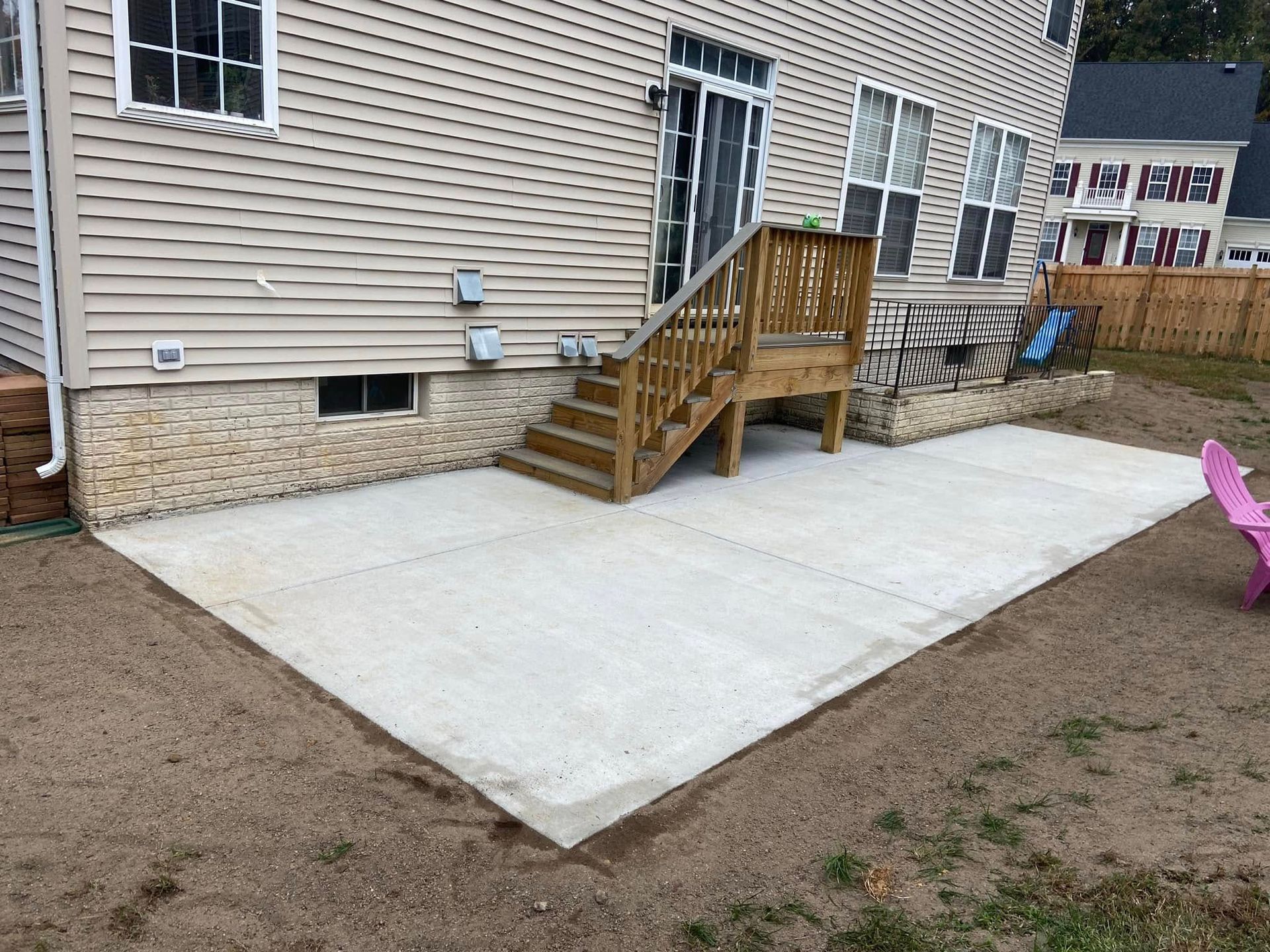 A concrete patio with stairs and a wooden deck in front of a house.