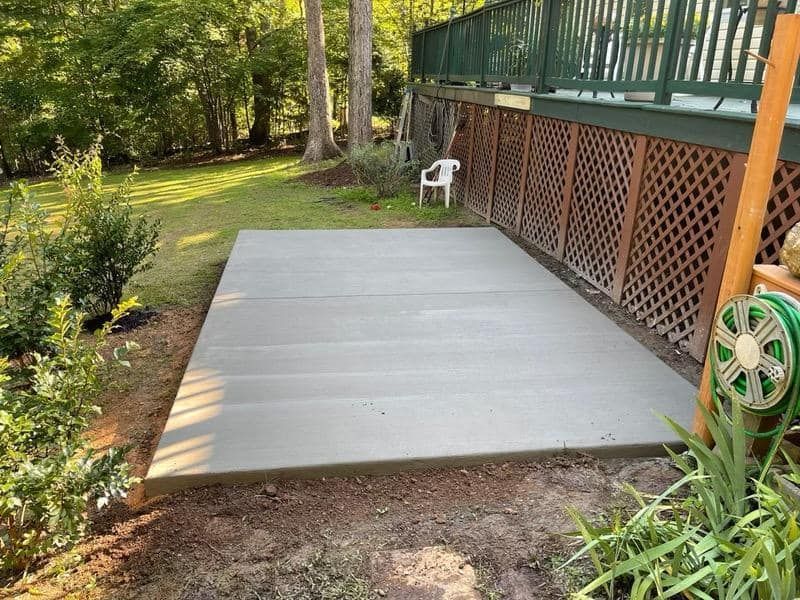 A concrete patio is being built in the backyard next to a deck.