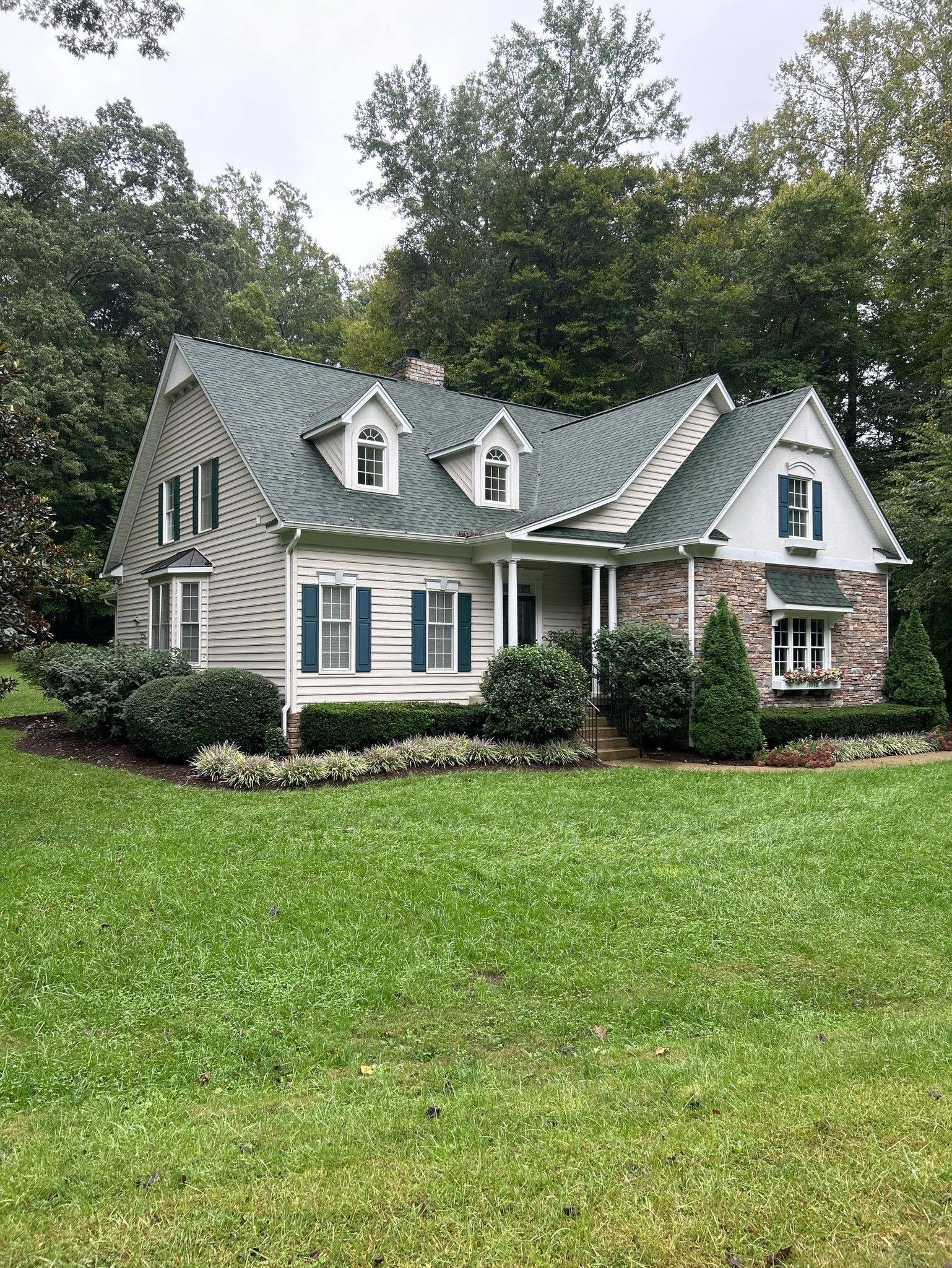 A house with a green roof and blue shutters is sitting on top of a lush green lawn.