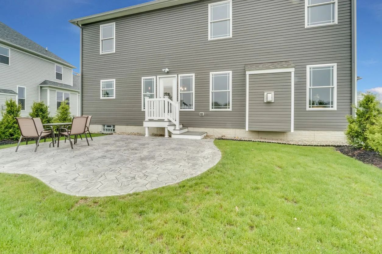Backyard patio with outdoor chairs, white door, and gray siding on a two-story house