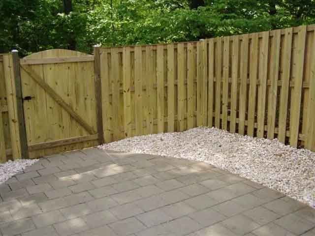 A wooden fence with a gate is surrounded by gravel and a patio.