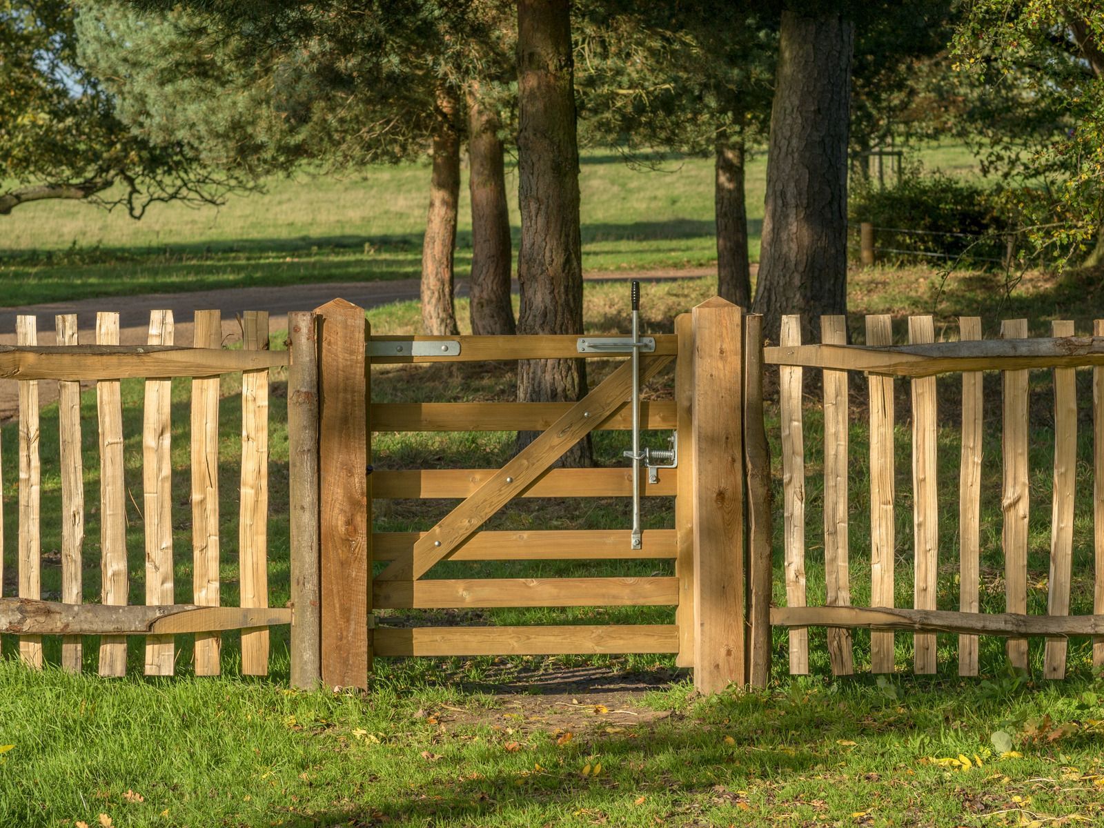 Wooden gate in a fenced grassy field with trees in the background