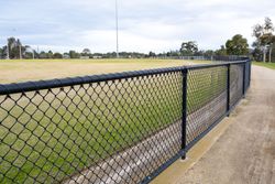 Chain-link fence bordering a grassy sports field beside a concrete path under a cloudy sky