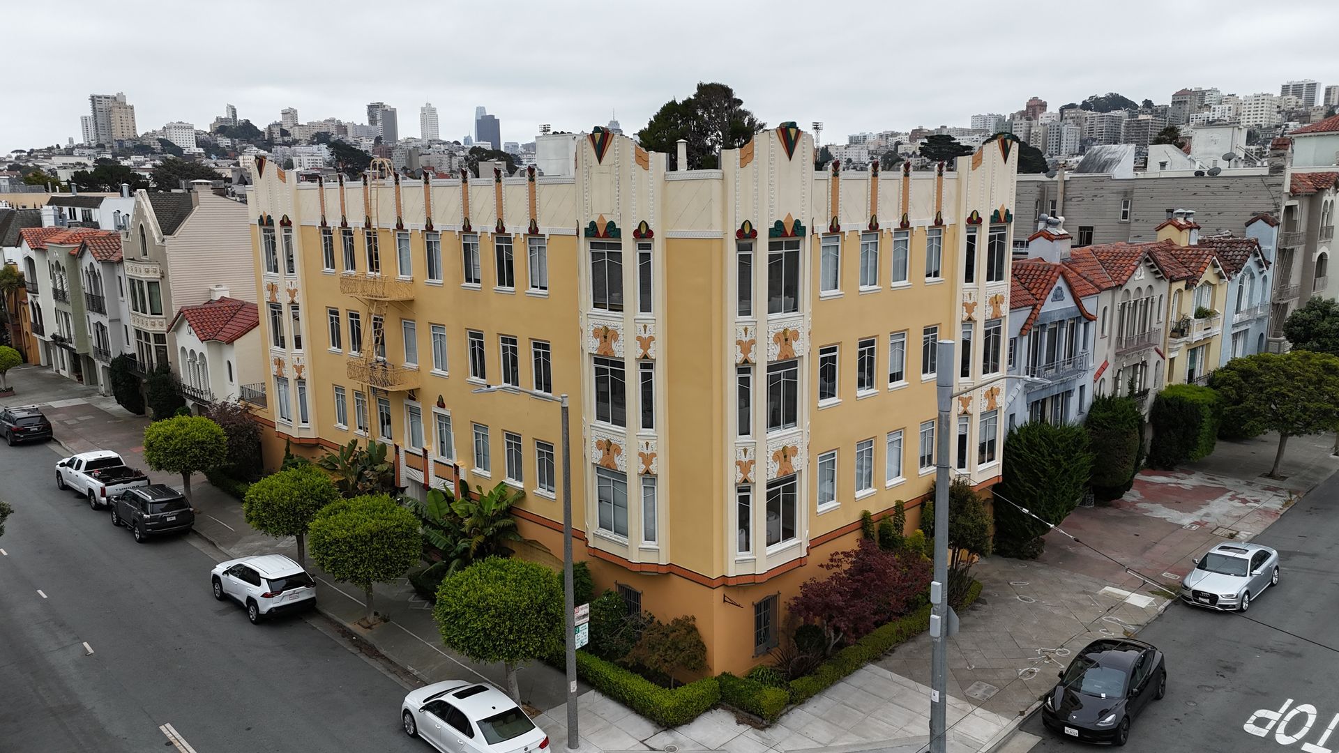 Corner view of a yellow apartment building on a city street with parked cars and overcast sky
