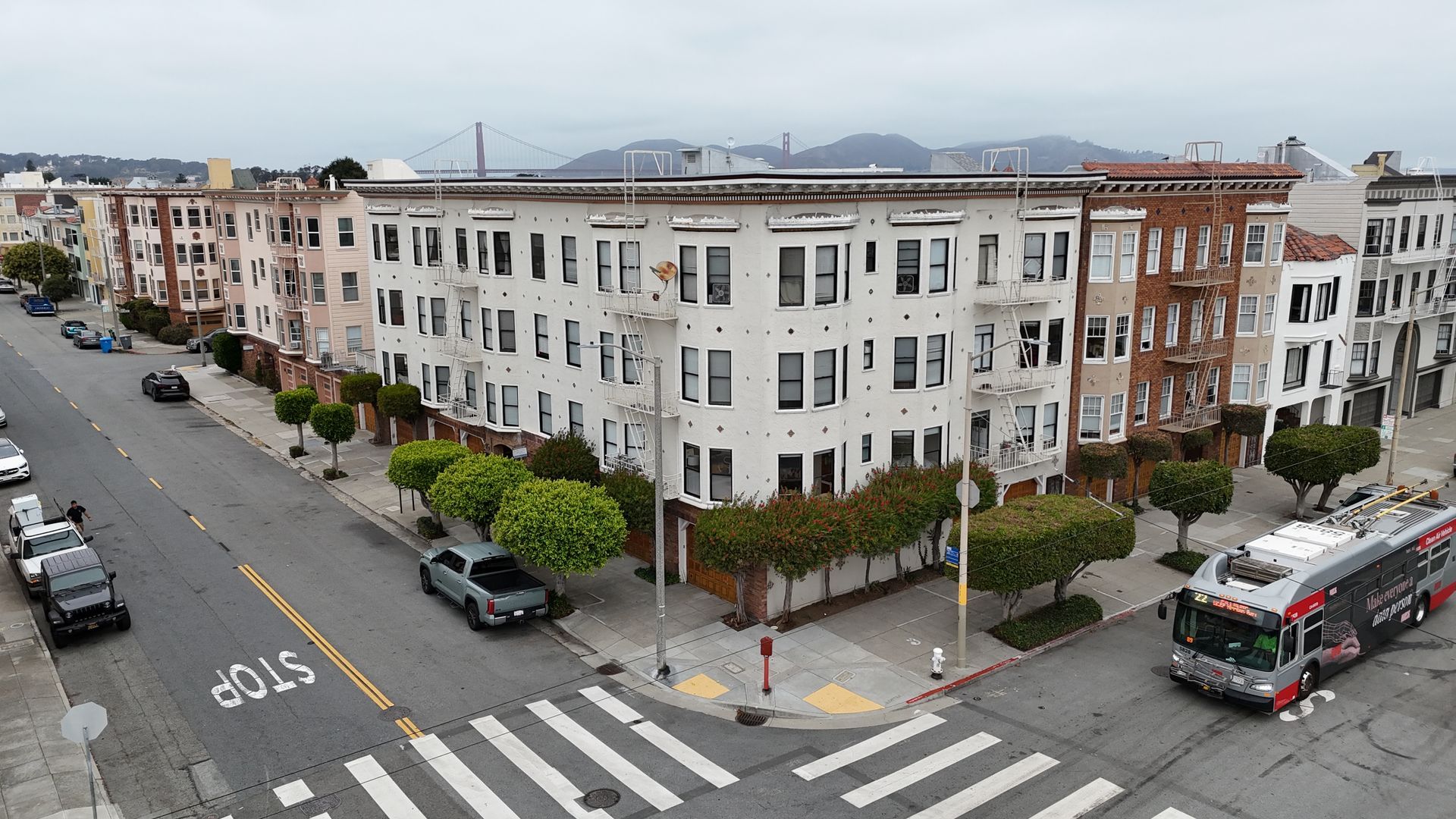 Intersection with a white apartment building, crosswalks, parked cars, and a city bus on a cloudy day