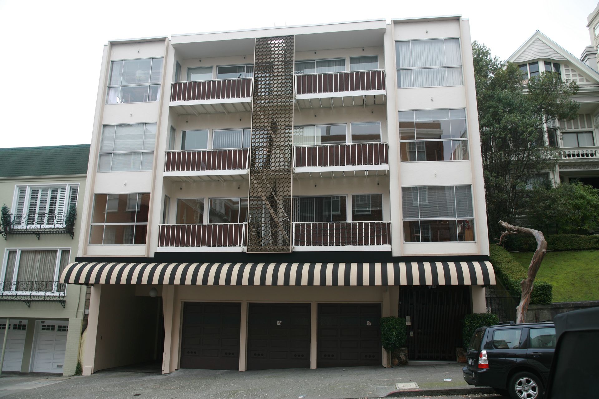 Four-story apartment building with striped awnings and balconies, viewed from the street