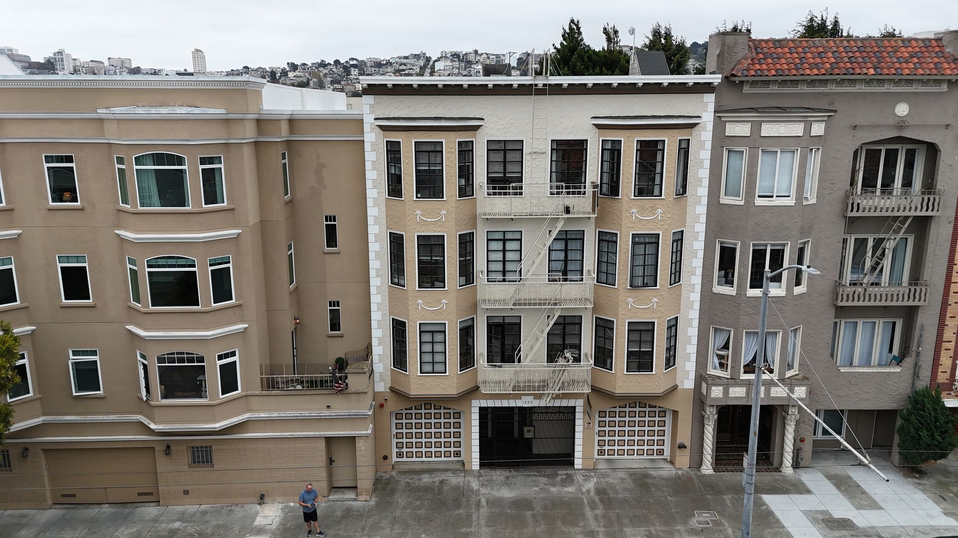 Row of beige apartment buildings with balconies and storefronts on a wet city street