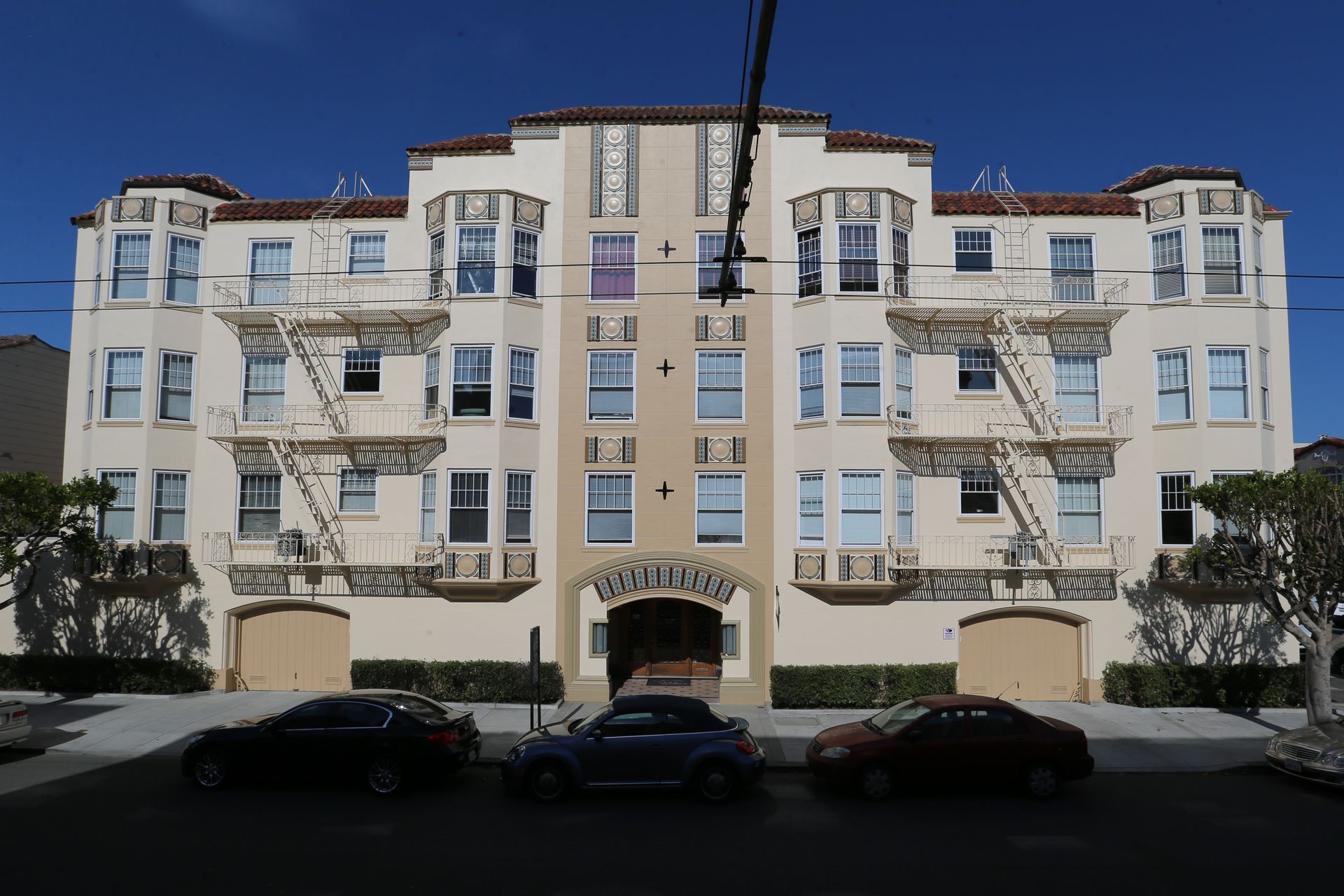 White apartment building with balconies and parked cars in front under a clear blue sky