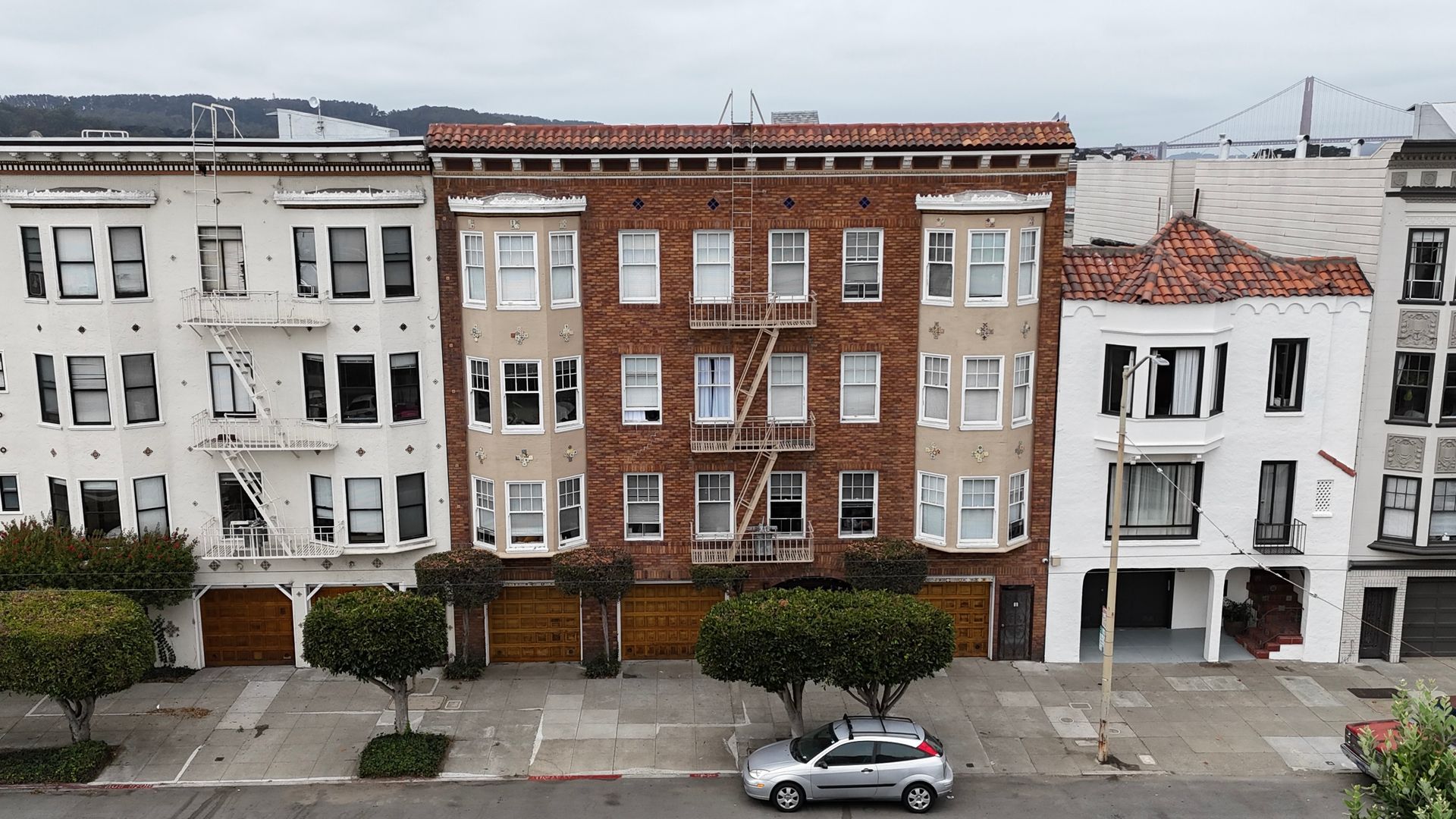 Row of urban townhouses with a parked silver car on a quiet street.