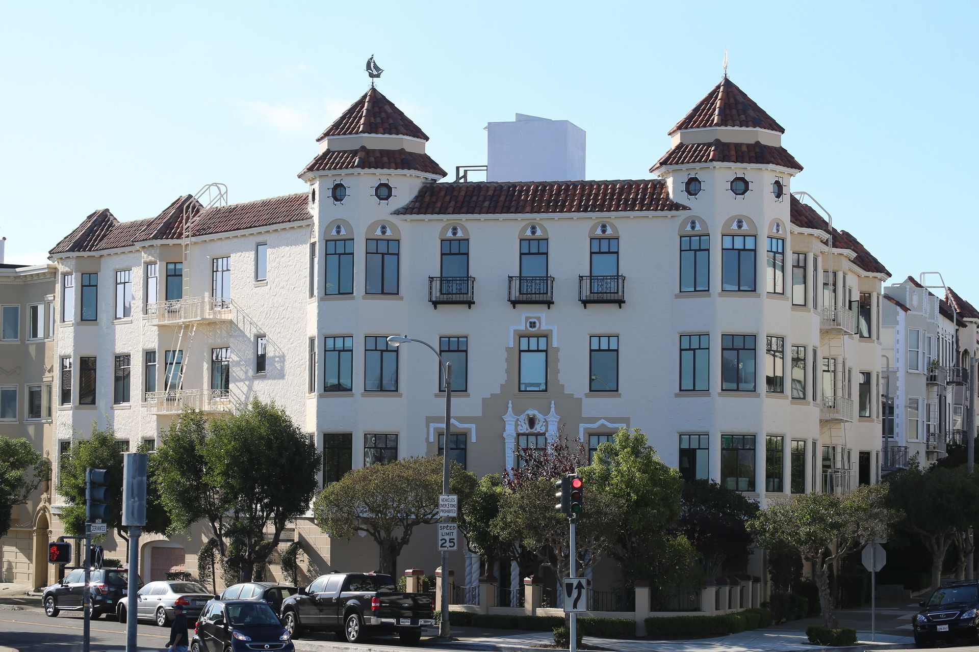 White Mediterranean-style apartment building with red-tiled roofs and balconies on a sunny street corner