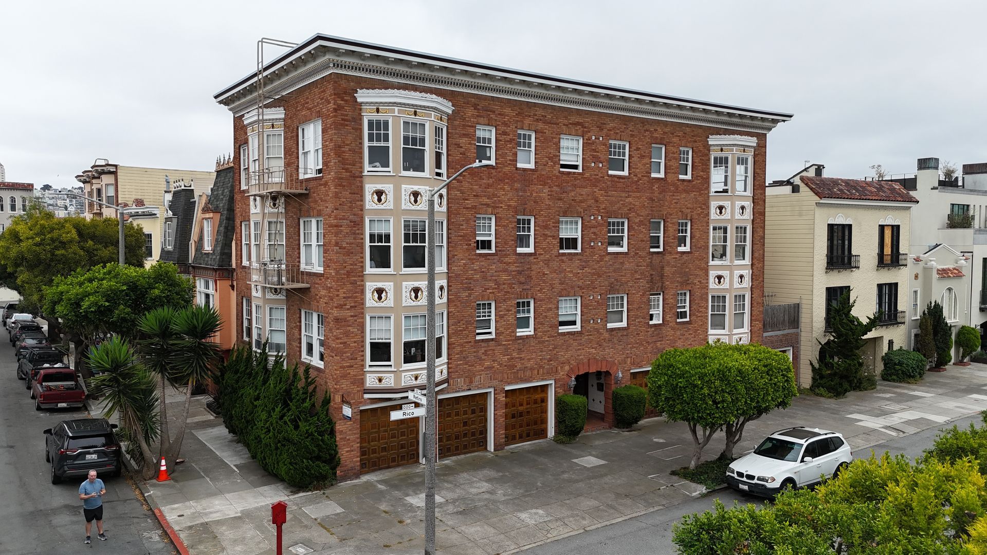 Brick apartment building on a street corner with parked cars and trees in a residential neighborhood