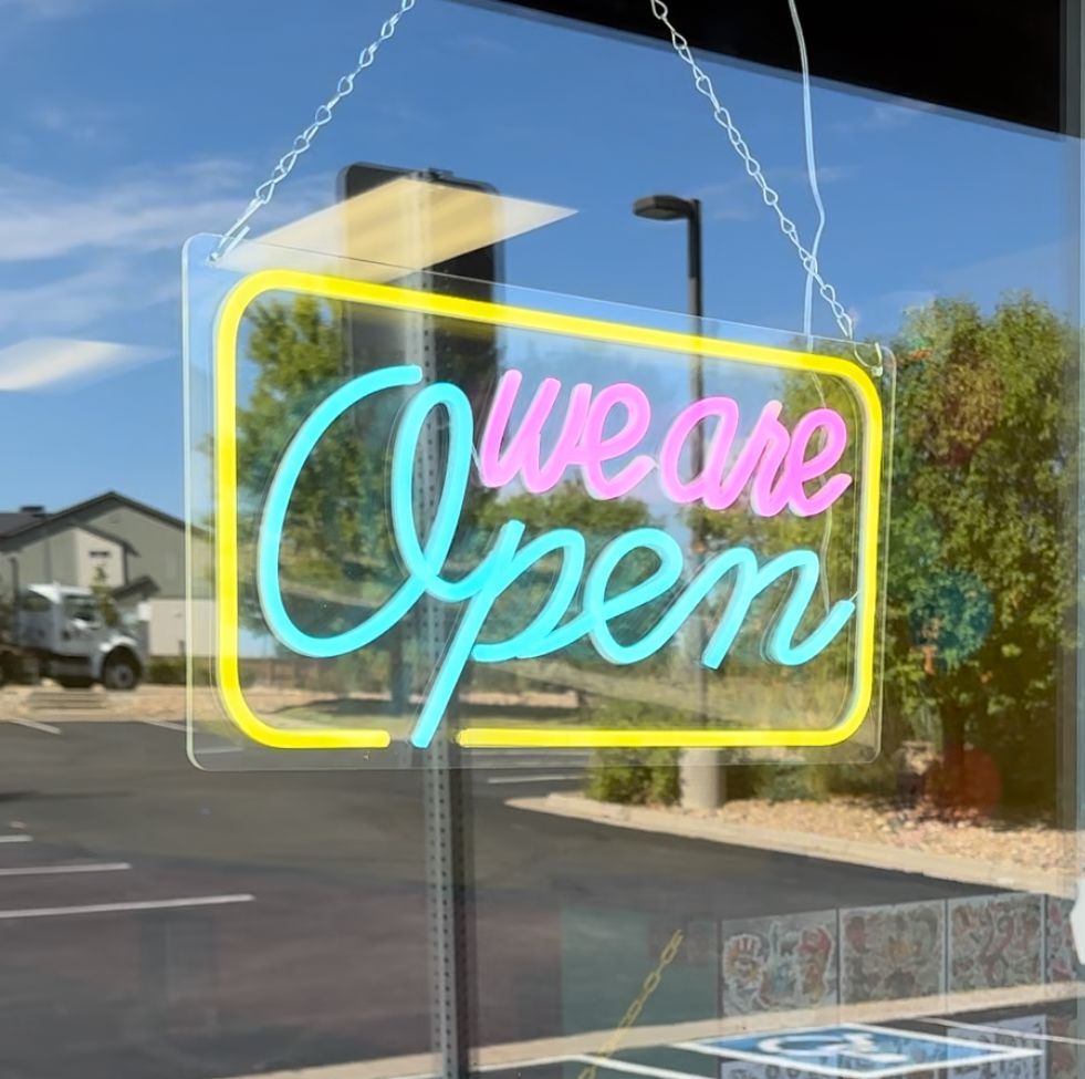 A neon sign that says we are open hangs in a window