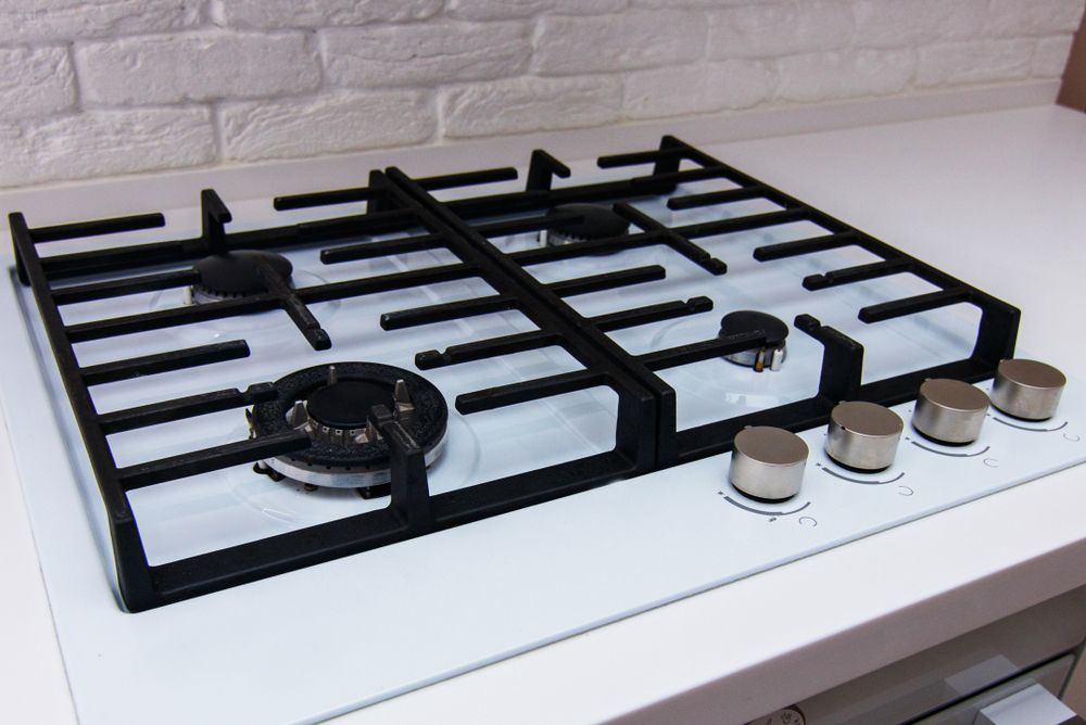 Gas Cooktop With Black Grates, Burners, and Silver Knobs on a White Surface — Carl Voss Electrical In Urangan, QLD