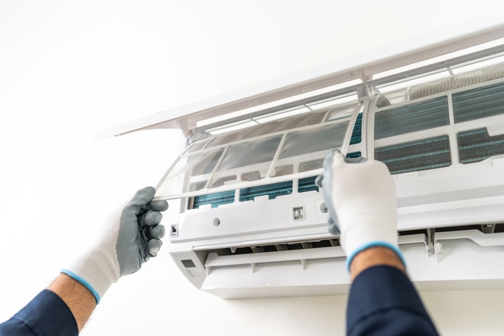 Hands Wearing Gloves Cleaning an Ac Unit Filter on a White Wall — Carl Voss Electrical In Urangan, QLD