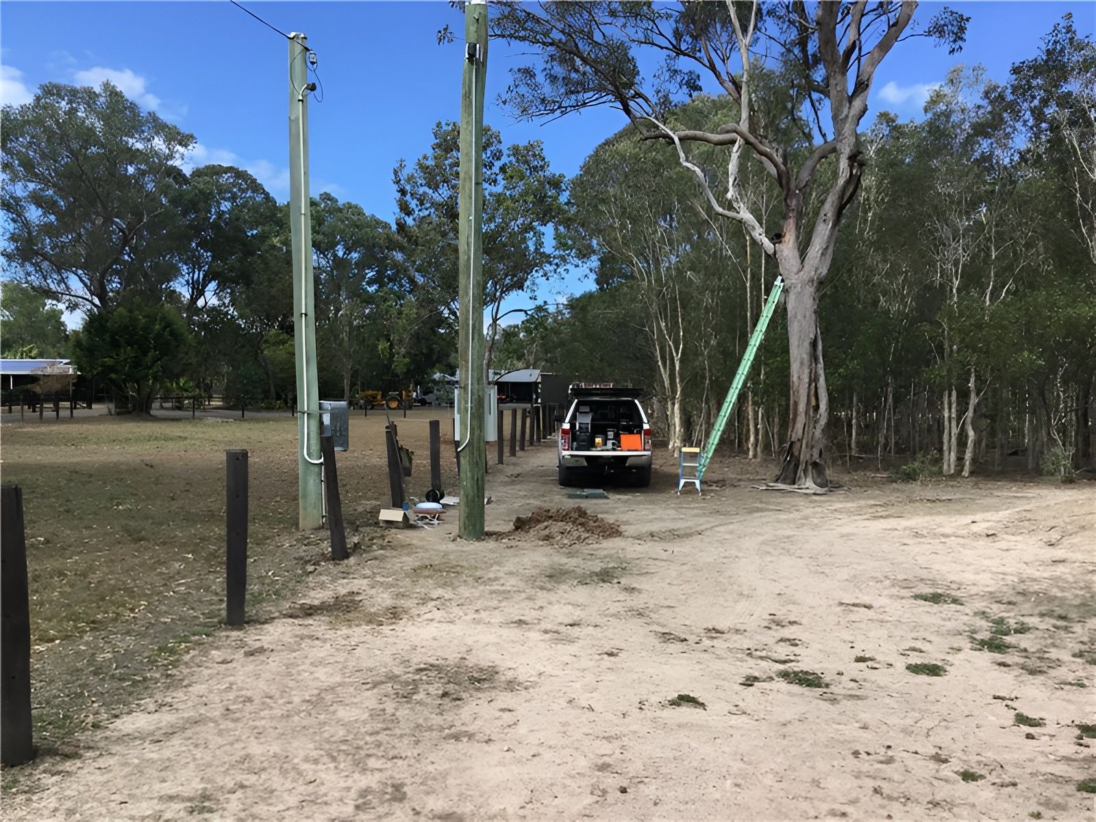 A Utility Truck Parked on a Dirt Road Near Power Poles and Trees — Carl Voss Electrical In Urangan, QLD