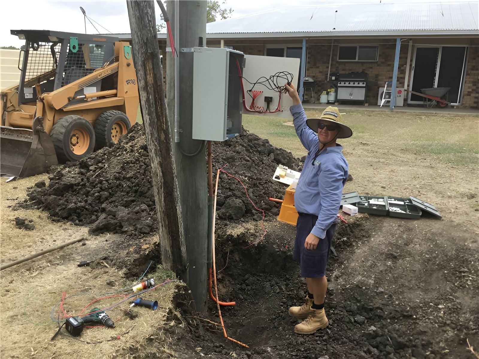 Man in Shorts by Utility Pole, Pointing at a Box — Carl Voss Electrical In Urangan, QLD