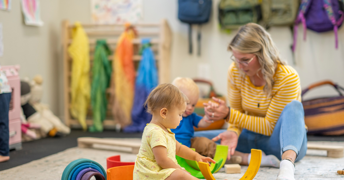 A woman is sitting on the floor playing with two children.