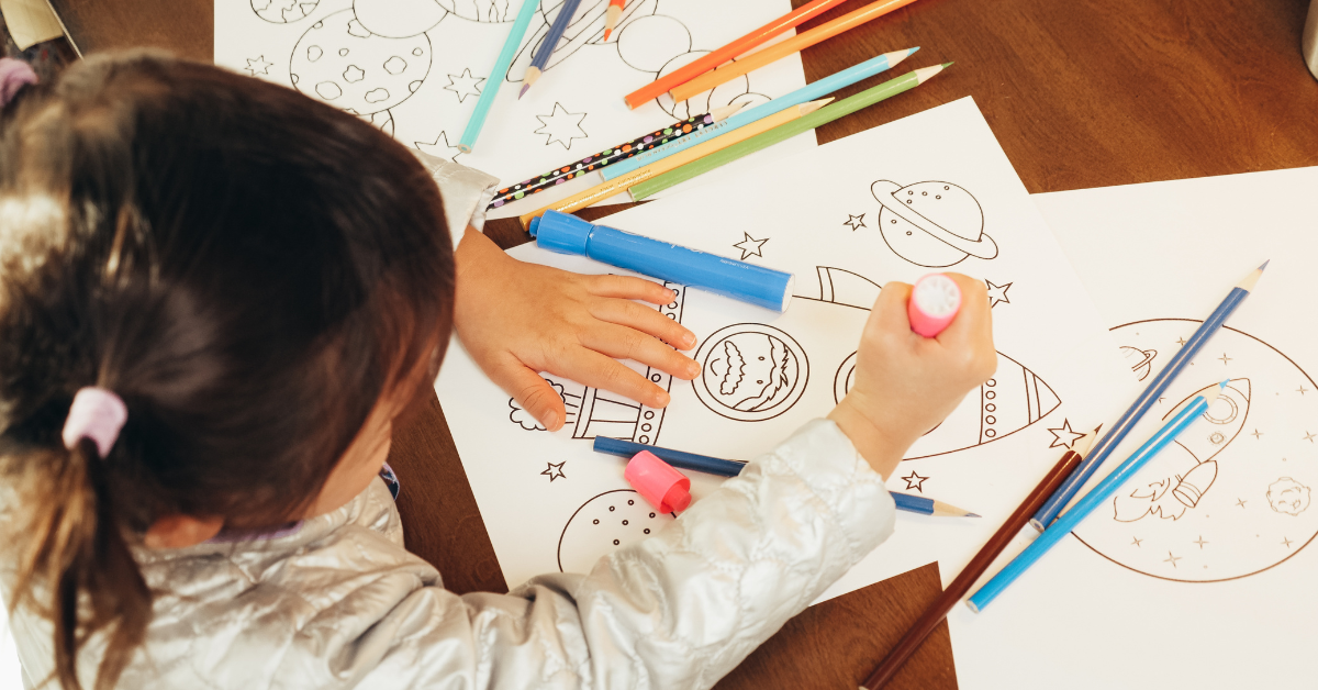 A little girl is sitting at a table drawing with markers and pencils.