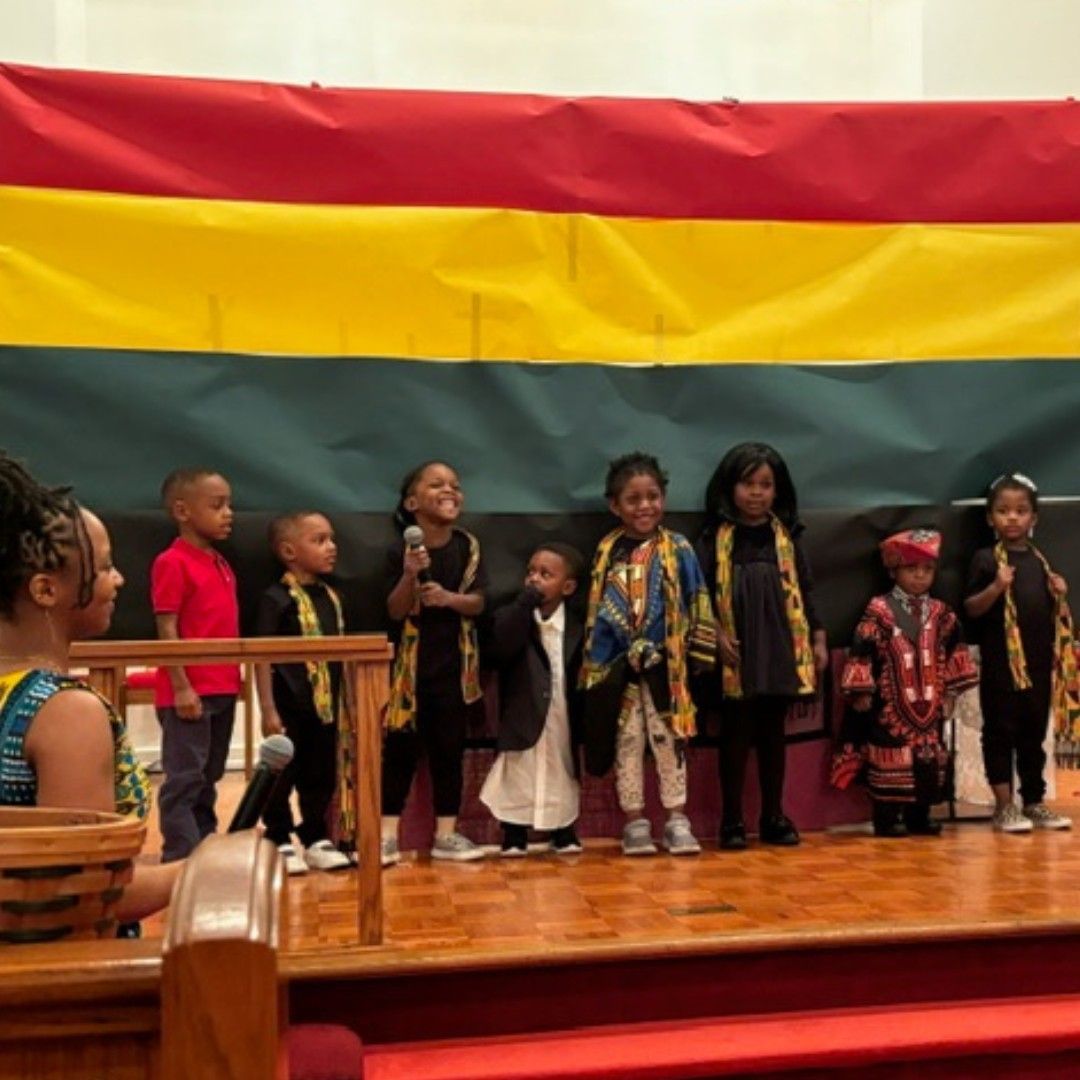 A group of children are standing on a stage in front of a flag