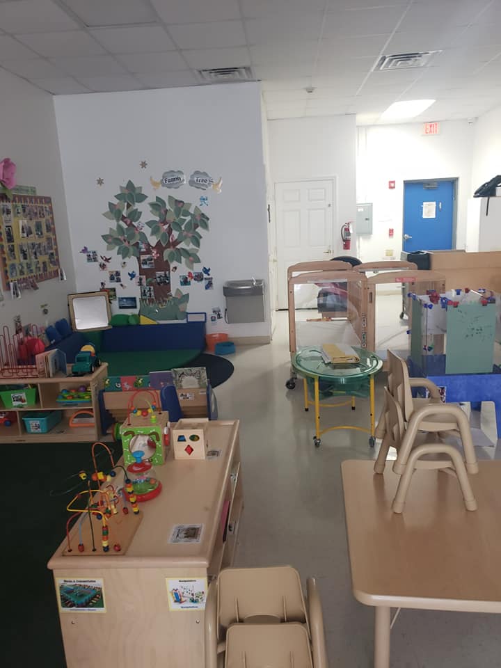 A classroom with tables and chairs and a tree on the wall.