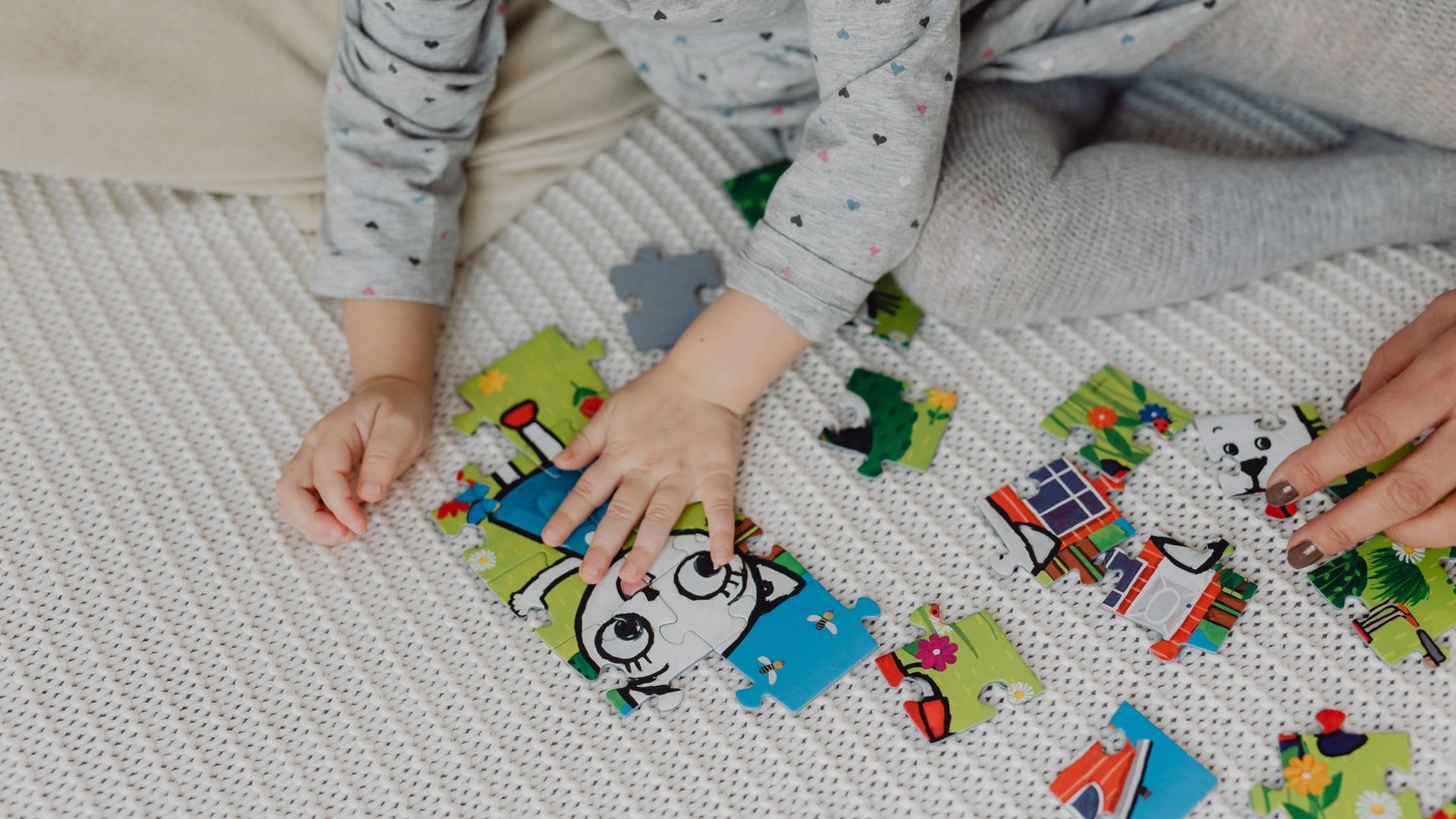 Child's hands playing with a colorful puzzle on a white knit blanket.