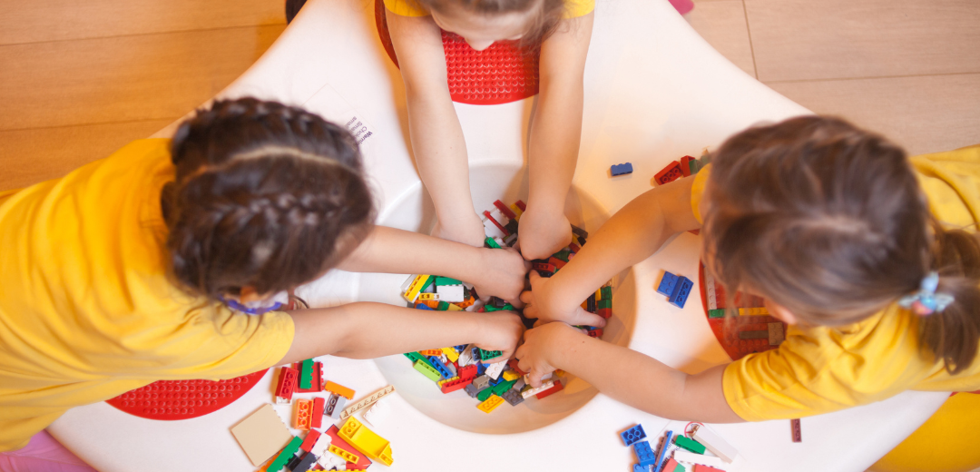 Three little girls are playing with lego blocks at a table.