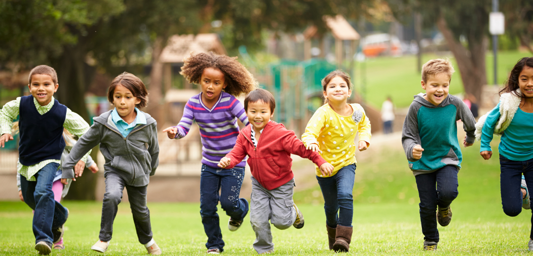 A group of children are running in a park holding hands.