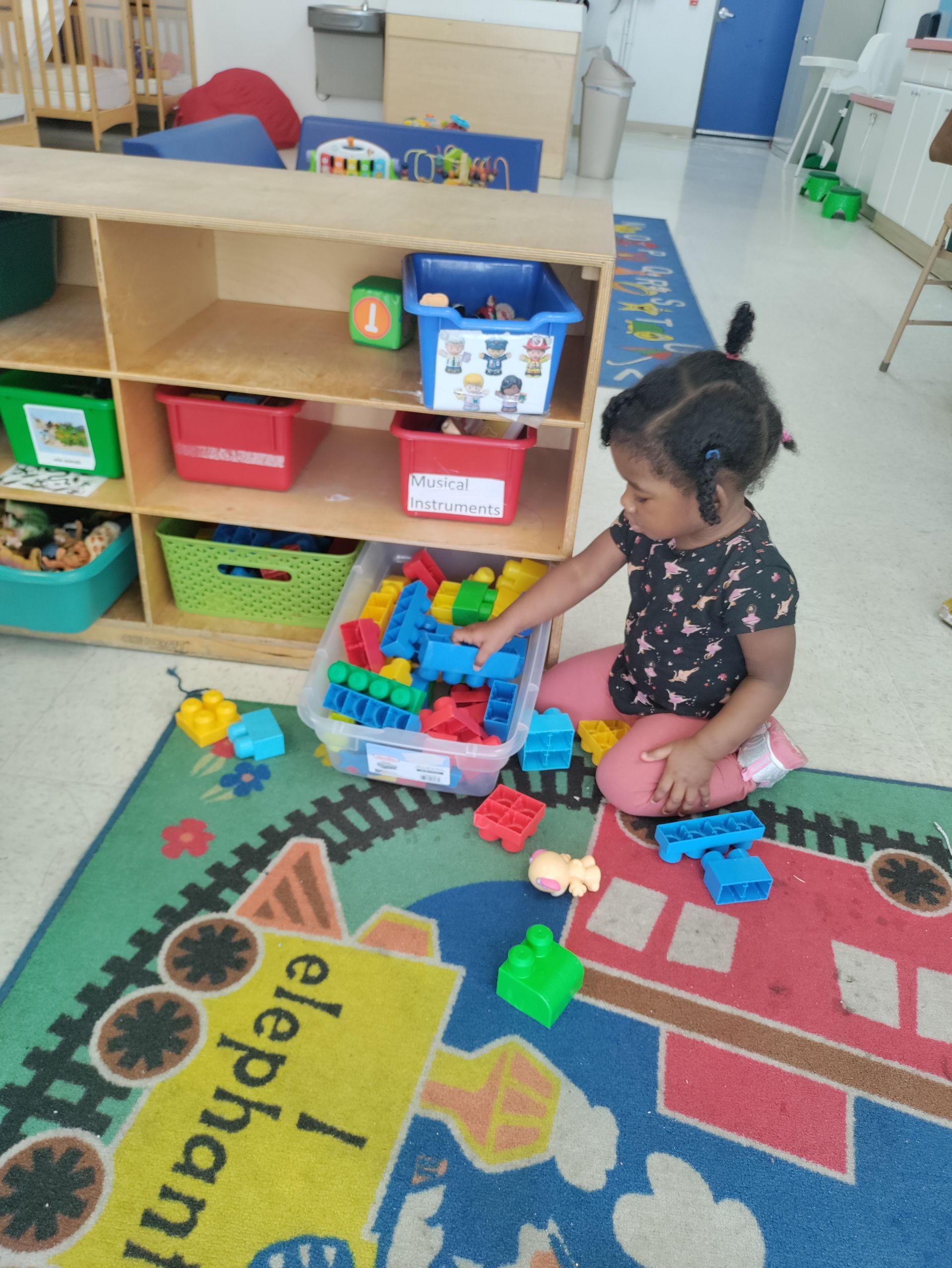A little girl is playing with blocks on a rug that says elephant