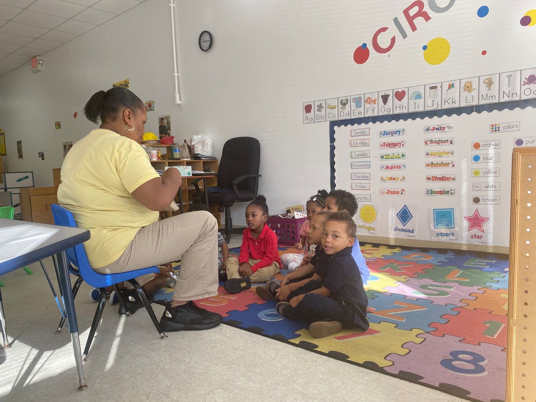 A woman is reading a book to a group of children in a classroom.