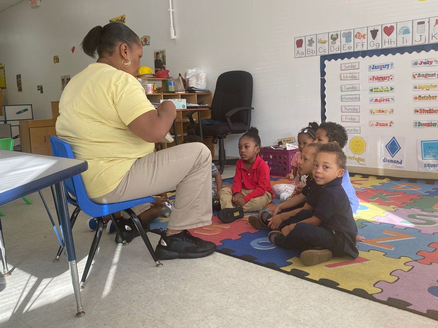 A woman is reading a book to a group of children in a classroom.