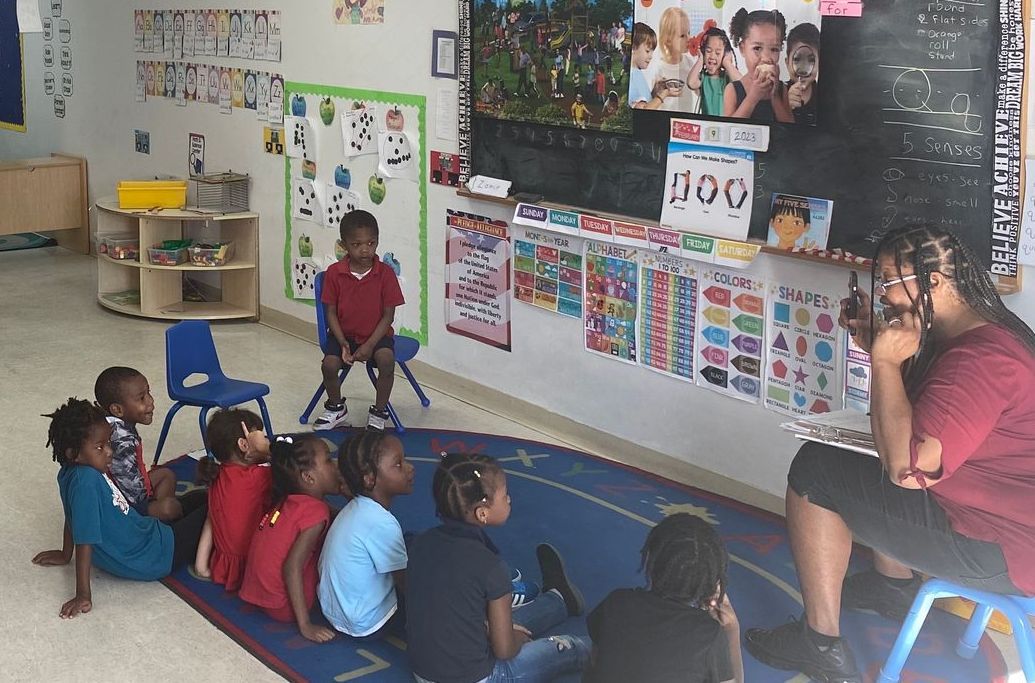 A woman is reading a book to a group of children in a classroom.