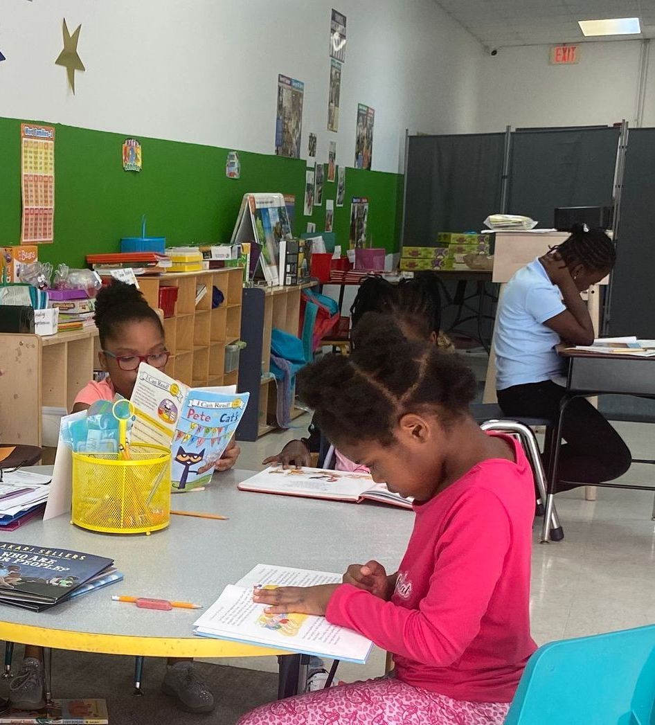 A girl in a pink shirt is reading a book in a classroom