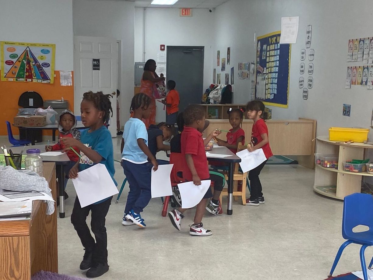 A group of children are standing in a classroom holding papers