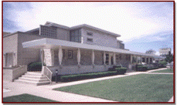 Modern building with a covered porch, stairs, and a green lawn under a cloudy sky