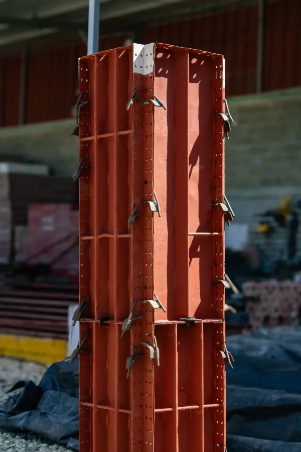 Columna de encofrado de plástico naranja en una obra de construcción, envuelta con alambres y bridas metálicas.