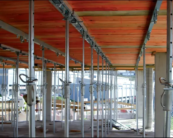 Obra en construcción con andamios metálicos, paneles de techo naranjas y estructura interior sin terminar.