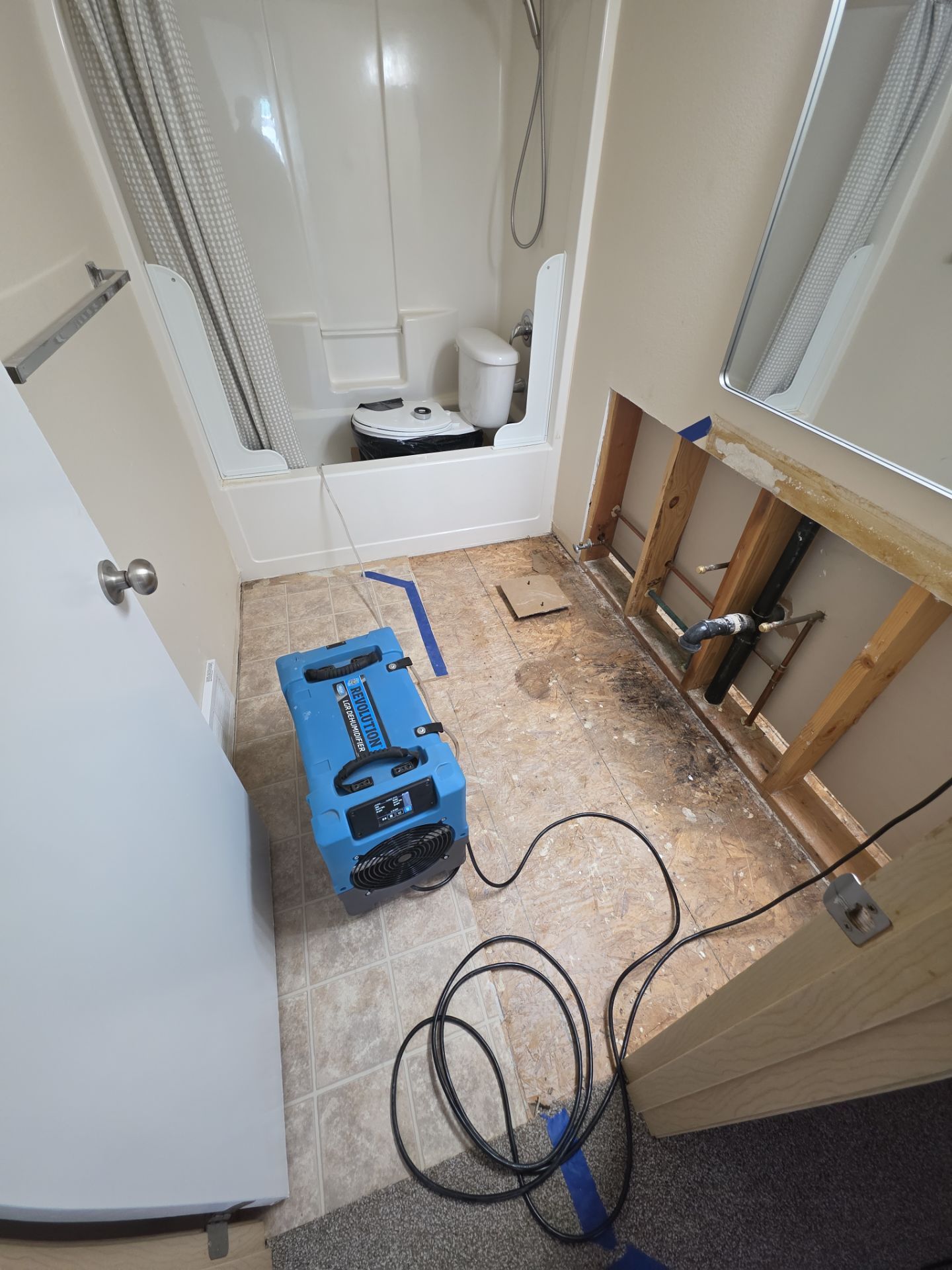 Small bathroom under repair with a blue dehumidifier, exposed wall studs, and a bathtub in the back.