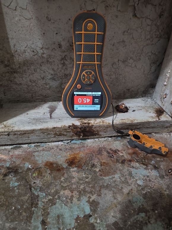 Orange-and-black handheld detector on a rough concrete ledge, with a small yellow tool beside it.