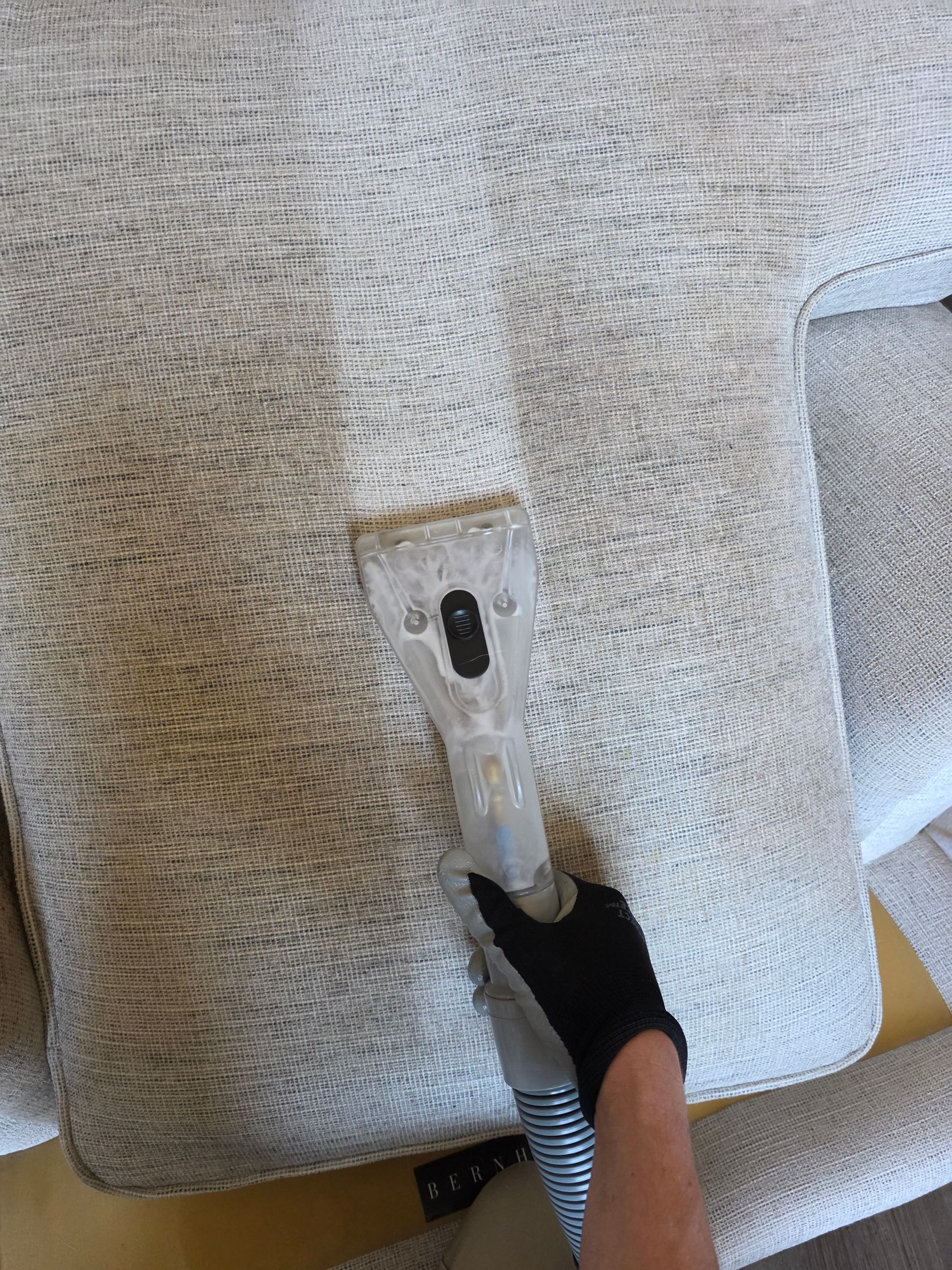 Hand in black glove pointing at a small tear and metal panel on a gray upholstered seat