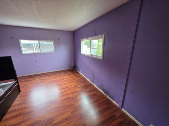 Empty purple room with hardwood floor and two windows letting in daylight